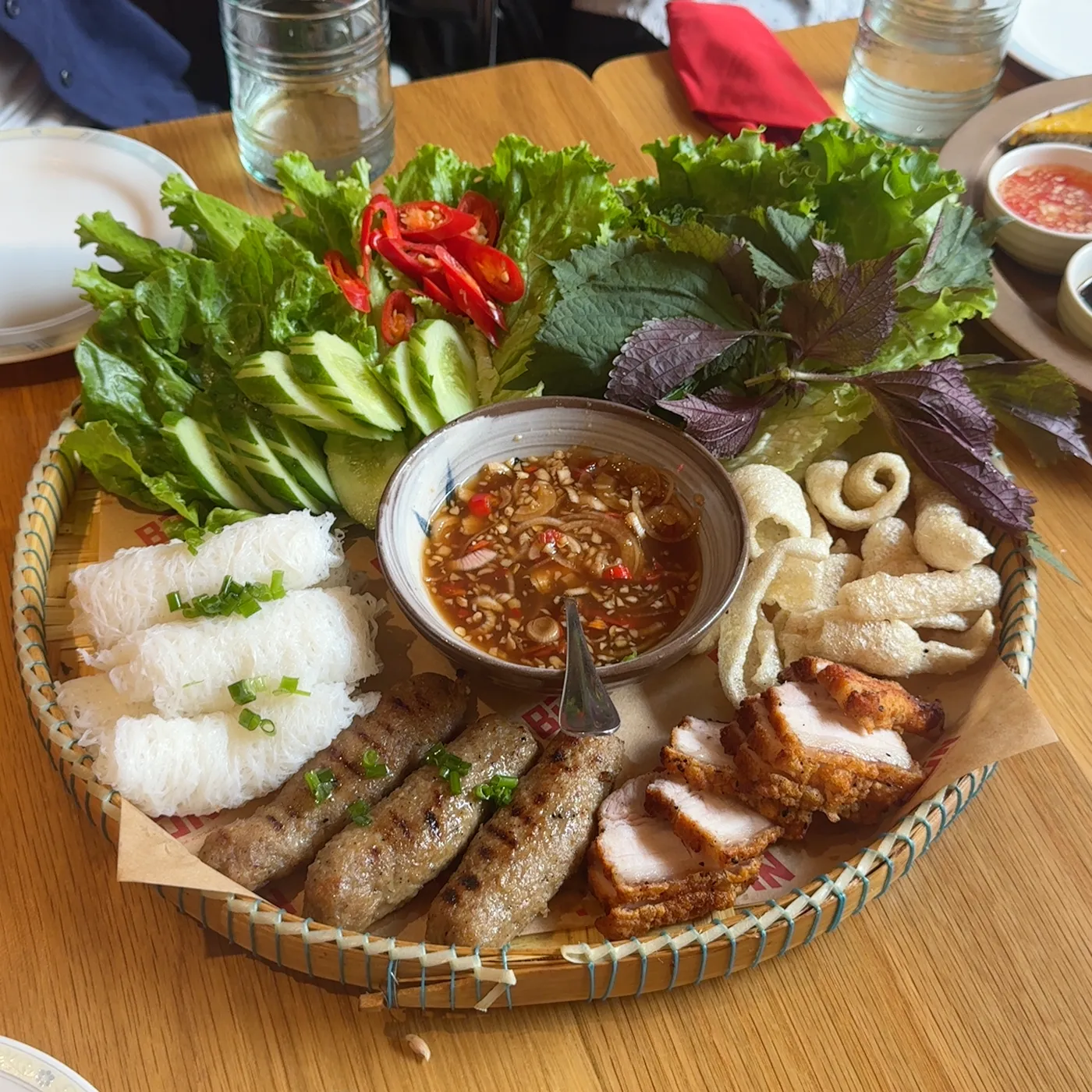Bánh hỏi platter with grilled meats, rice paper and a basket of fresh herbs